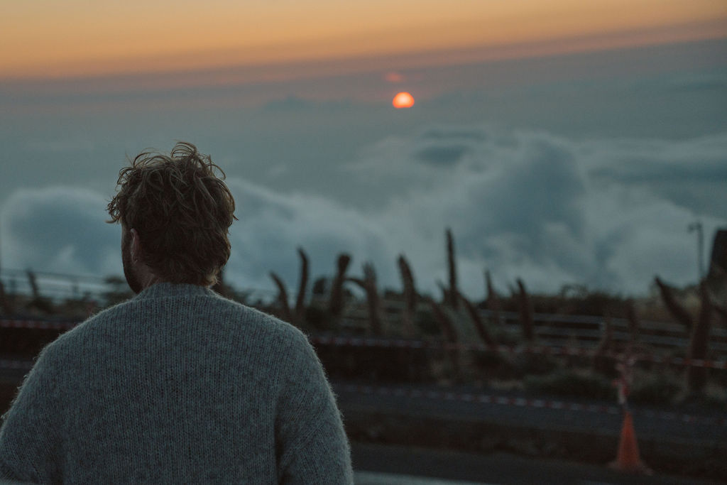 Ein Mann im Wollpullover blickt vom Bergpass auf das Wolkenmeer im Sonnenuntergang