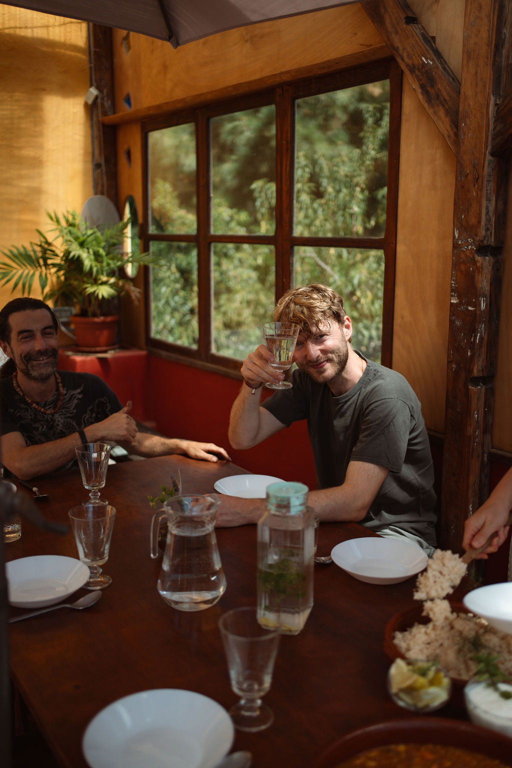 Zwei Teilnehmende sitzen am langen Tisch der Ecofinca Miraflores und heben ihre Gläser