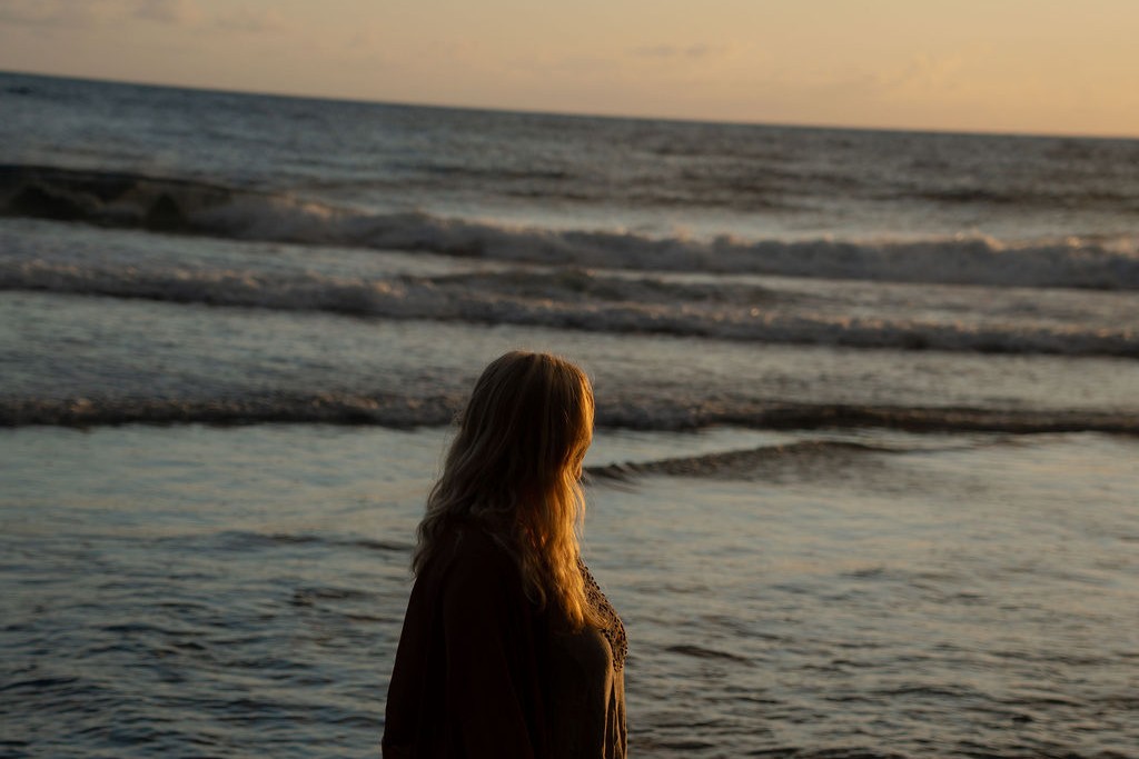 Julia steht im warmen Abendlicht am dunklen Strand und blickt auf das Meer